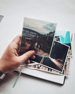 A person holding photos with a vintage camera and notebook on a desk.